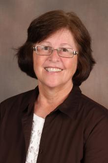 Marla Reicks wearing glasses, a white blouse and a brown shirt on top 